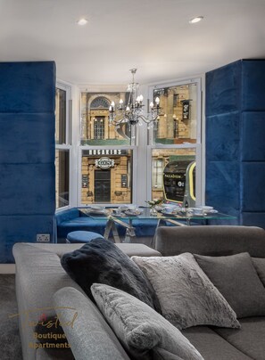 Un salon moderne avec une table en verre, des canapés bleus et un lustre.