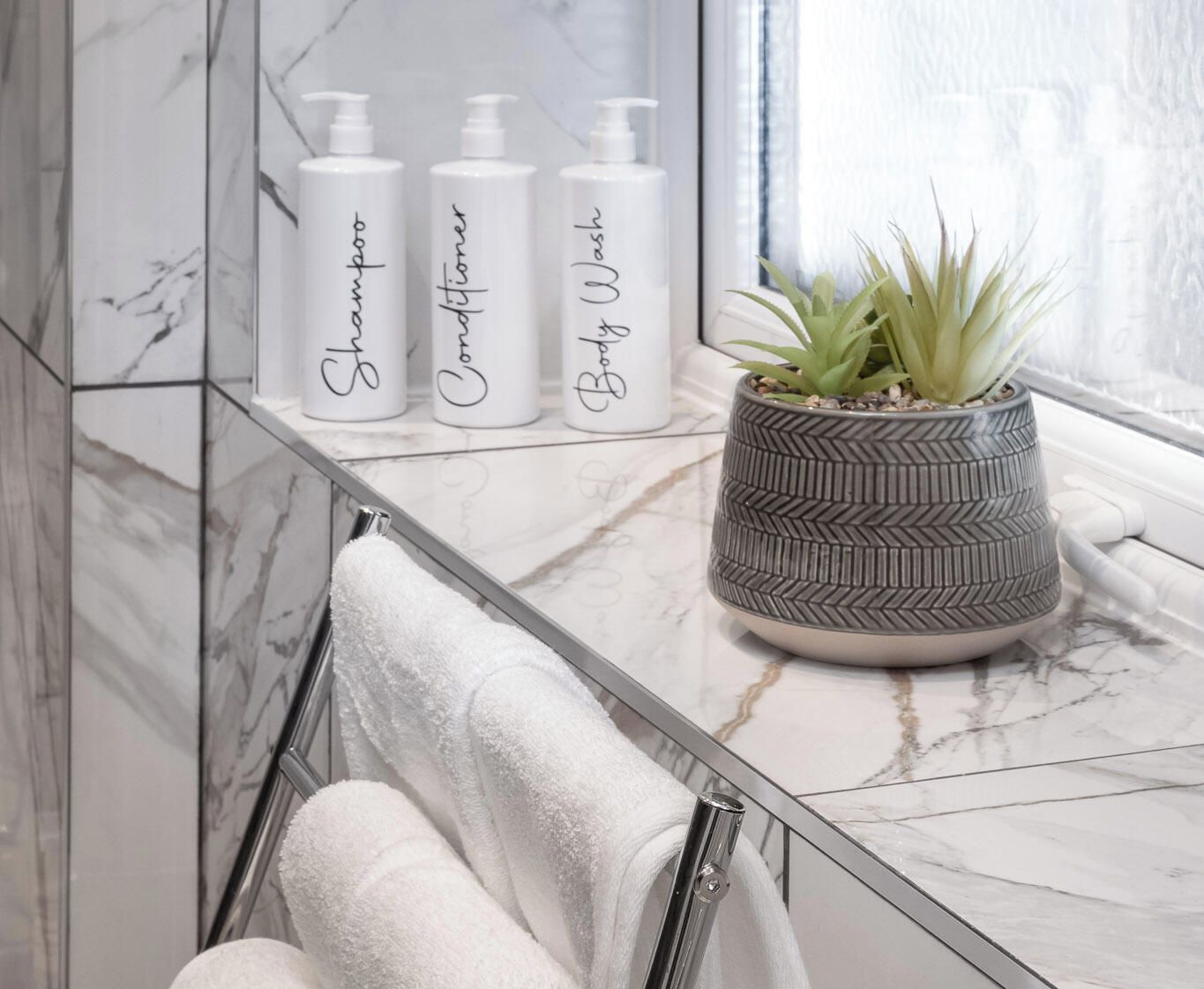 A bathroom with a marble countertop, three toiletry bottles, a potted plant, and a towel rack.
