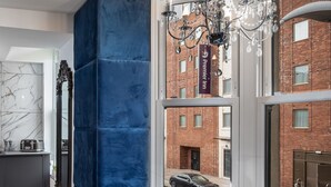 Un espace repas moderne avec une table en verre pouvant accueillir six personnes, un mur d’accent bleu et une vue sur un bâtiment en briques à l’extérieur.