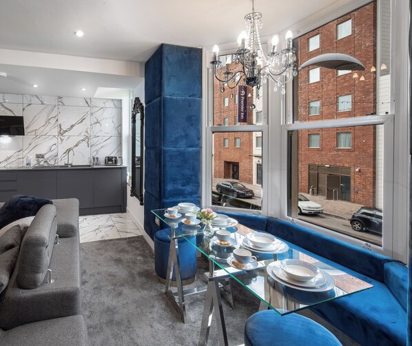 Un salon moderne avec un canapé gris, une table basse en verre et une vue sur un bâtiment en briques, visible à travers de grandes fenêtres.