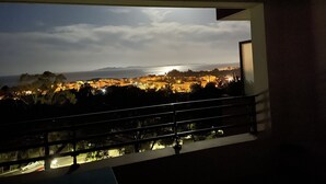 Ein Balkon mit Blick auf eine beleuchtete Stadtlandschaft, darunter Gebäude und ein Gewässer.