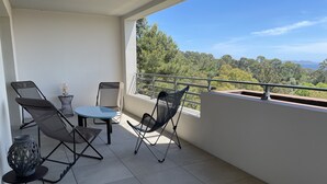 Ein Balkon mit Tisch und Stühlen, ein kleiner Beistelltisch mit einer Vase sowie Blick auf Bäume und Berge.