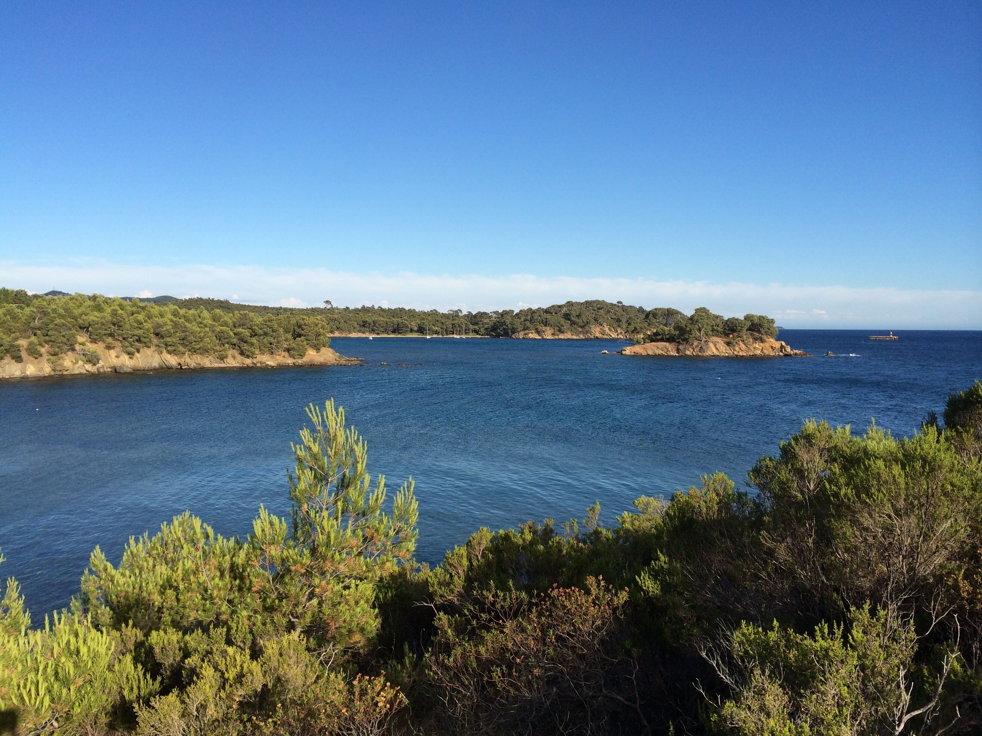 A coastal landscape with clear blue waters, a hilly backdrop, and dense greenery.