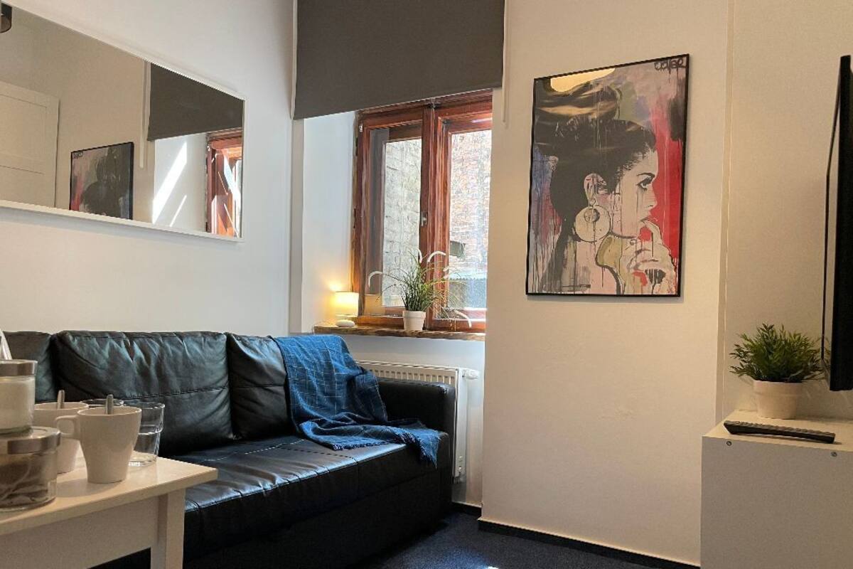 A modern living room with a black leather sofa, a white coffee table, and a painting on the wall.
