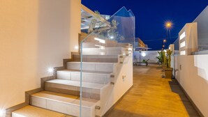 Una escalera moderna con barandillas de vidrio que conduce a un nivel superior, rodeada de paredes blancas y un piso de madera.