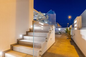 A modern staircase with glass railings leading to an upper level, surrounded by white walls and a wooden floor. - Appartamento Malika Rosso - Torr... (Taviano)
