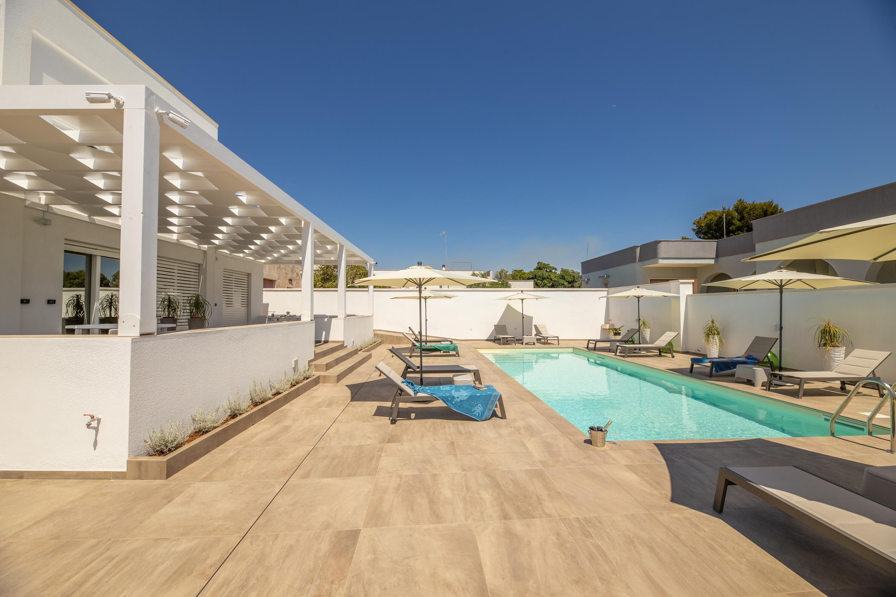 A modern outdoor pool area with lounge chairs, umbrellas, and a clear blue sky.