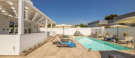 A modern outdoor pool area with lounge chairs, umbrellas, and a clear blue sky.