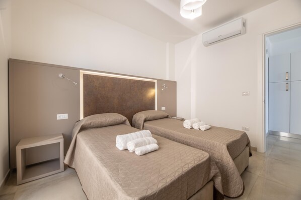 A hotel room with two beds, a bedside table, and an air conditioning unit.