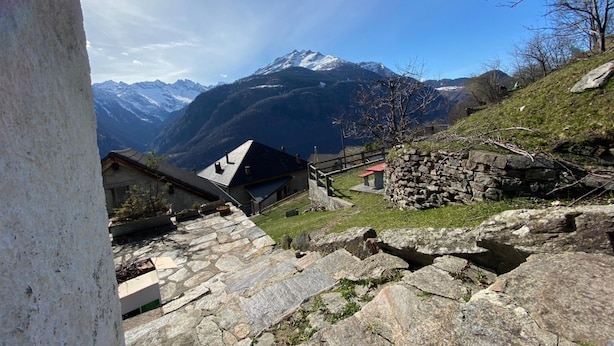 A stone staircase leading to a building with a sloped roof, surrounded by a stone wall and a view of snow-capped mountains. - Two-bedroom apartment with mountain view and garden (SANTORINI) (Anzonico)