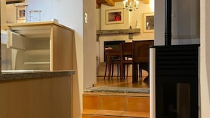 A kitchen with a built-in oven, a dining area with chairs, and a fireplace. - Two-bedroom apartment with mountain view and garden (SANTORINI) (Anzonico)