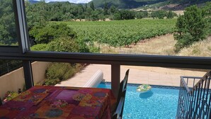 A balcony with a table covered in a floral tablecloth, a pool, and a vineyard view.