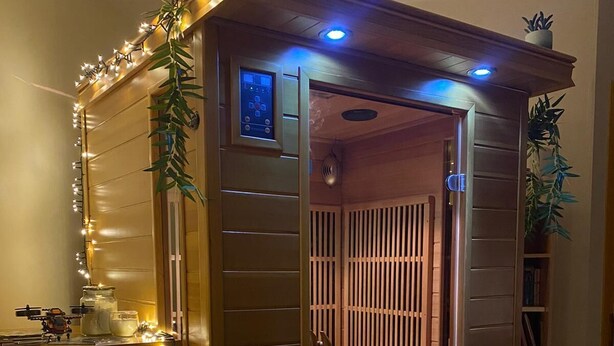 A sauna with a control panel, wooden slats, and a bench.