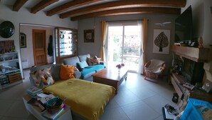 A cozy living room with a sofa, a coffee table, and a TV. There is a bookshelf and a window with curtains.