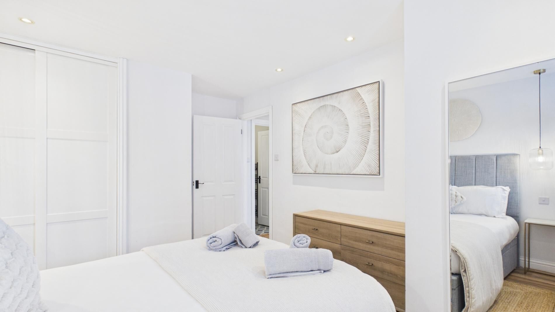 A bedroom with a bed, a wooden dresser, a wall art piece, and a door.