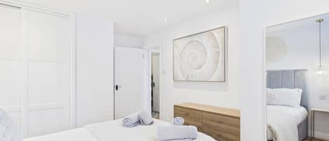 A bedroom with a bed, a wooden dresser, a wall art piece, and a door.