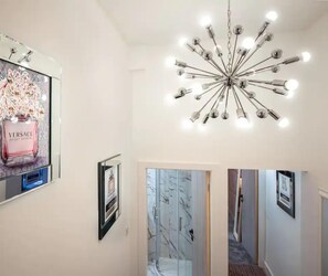 A hallway with a mirrored wall, a chandelier, and framed pictures.