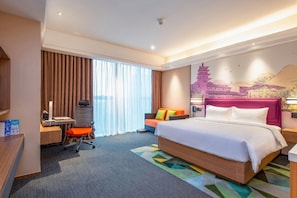 A hotel room with a bed, desk, chair, and a large window with curtains.