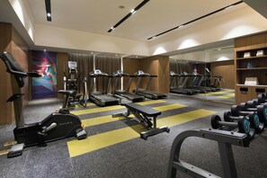 Ein Fitnessraum mit Laufbändern, Crosstrainern, einer Langhantelbank und Kurzhanteln.