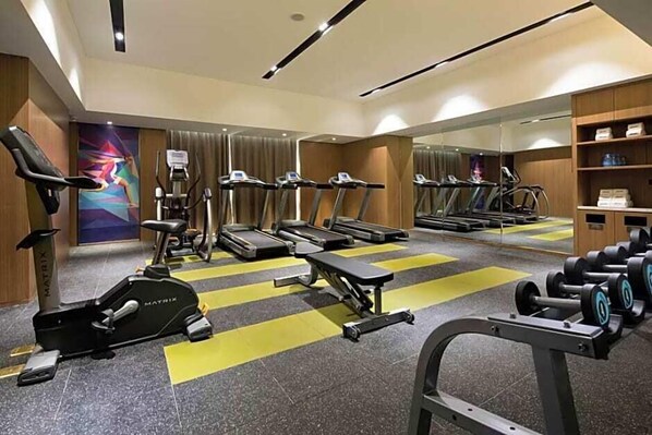 Un gimnasio con cintas de correr, una elíptica, una prensa de banca y mancuernas.