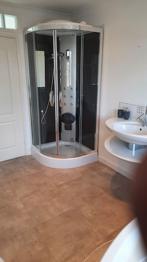 A modern bathroom with a glass-enclosed shower, a white sink, and a tiled floor.