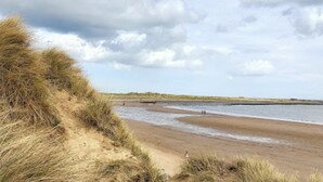 Een strand met duinen en een rustige zee.