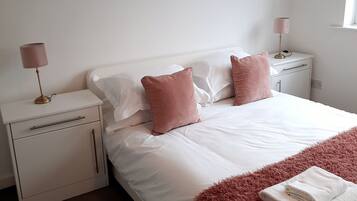 Quarto com uma cama grande, duas mesas de cabeceira, um criado-mudo, um abajur e um quadro na parede.