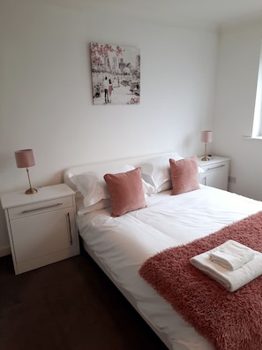 A bedroom with a large bed, two bedside tables, a nightstand, a lamp, and a painting on the wall.
