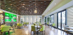 A modern dining area with wooden flooring, green chairs, and a green-lit wall display. - Hampton BY Hilton Suzhou NEW District (SUZHOU)