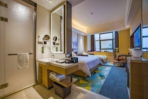 A hotel room with a bed, a desk, a chair, a large mirror, a window, and a bathroom with a sink and towel rack. - Hampton BY Hilton Suzhou NEW District (SUZHOU)