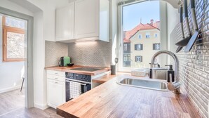 A modern kitchen with white cabinets, a wooden countertop, a built-in stove, and a view of a red-roofed building through a large window.