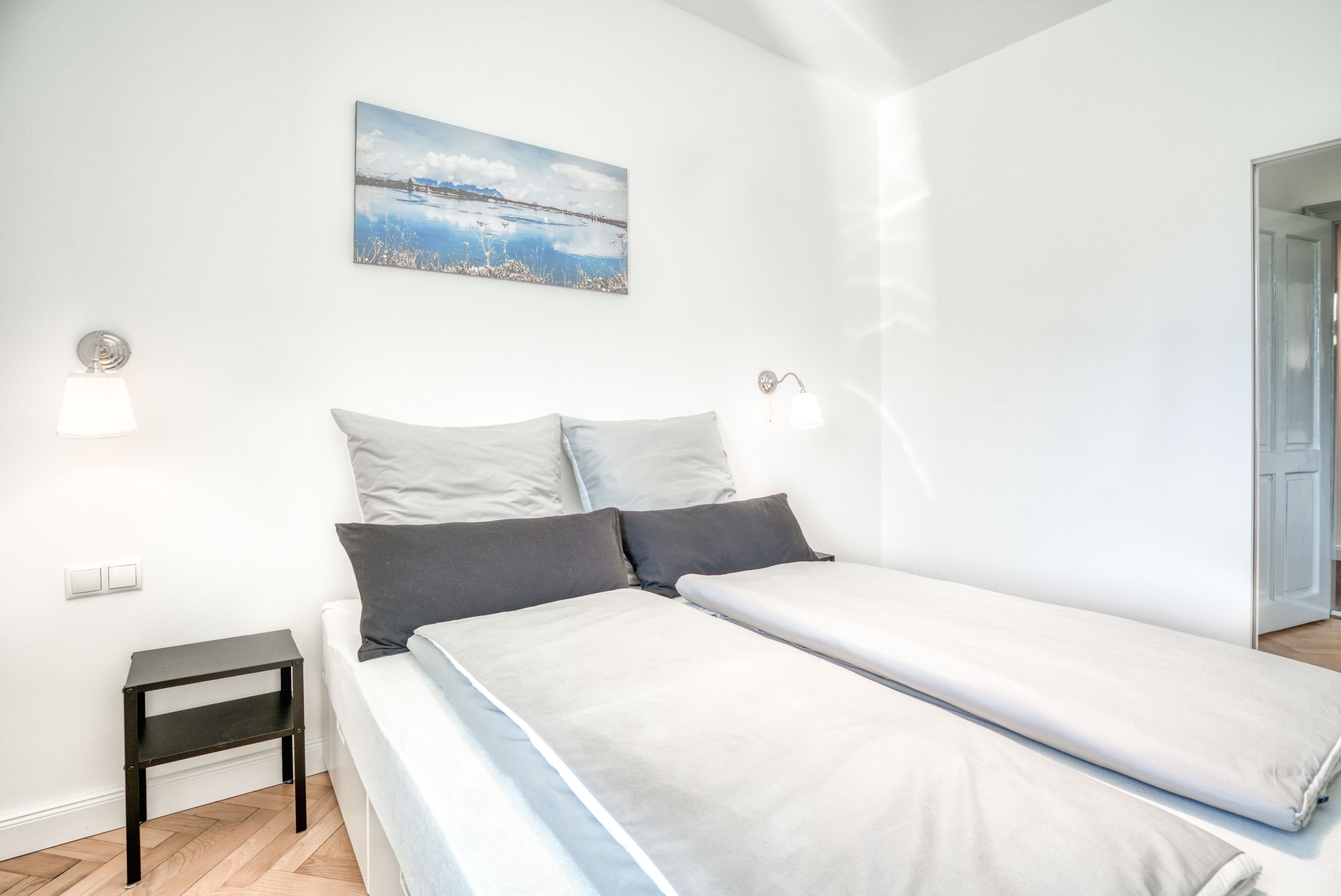 A bedroom with a bed, a nightstand, a wall-mounted lamp, and a painting.