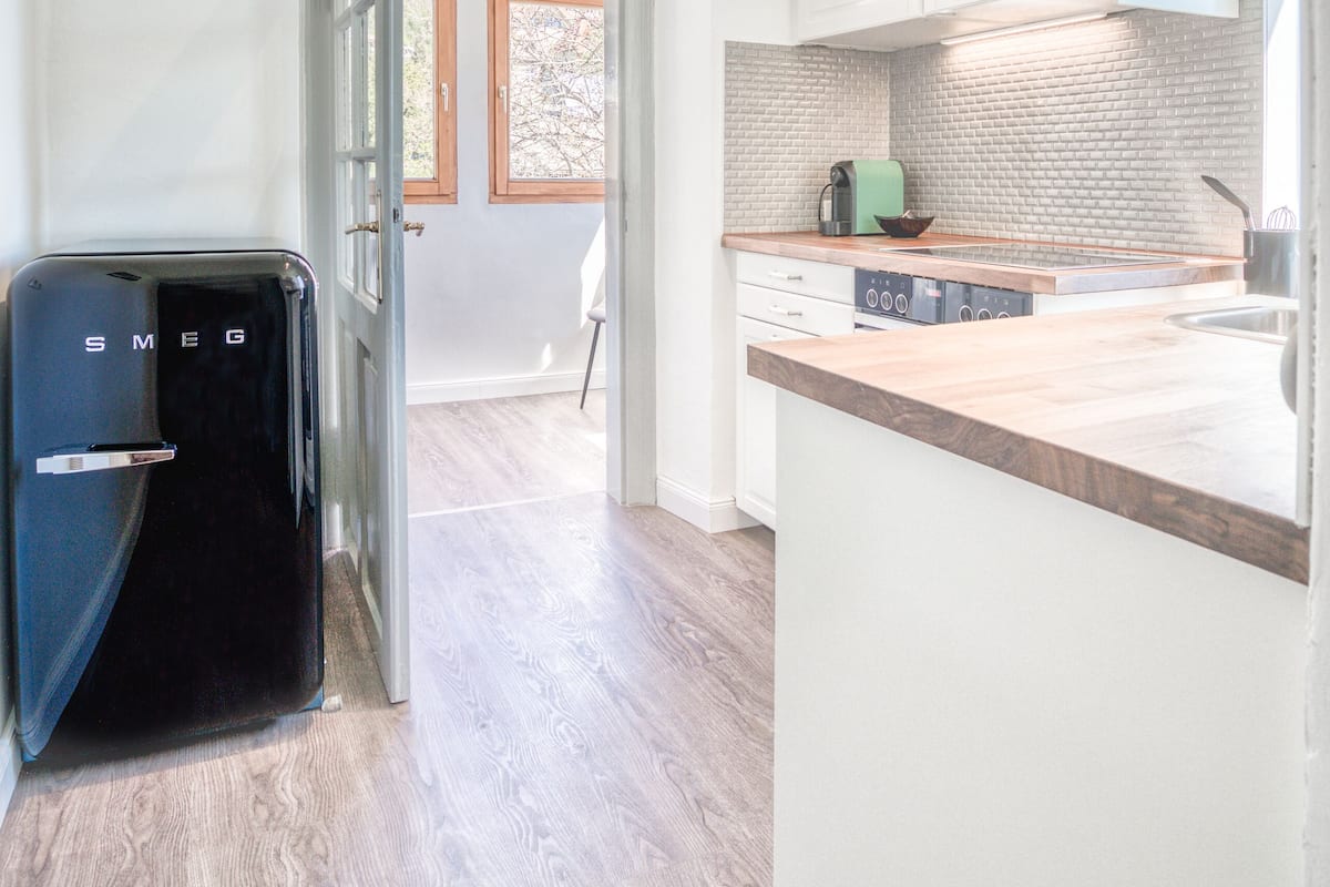 Una cocina moderna con armarios blancos, encimera de madera y horno empotrado.