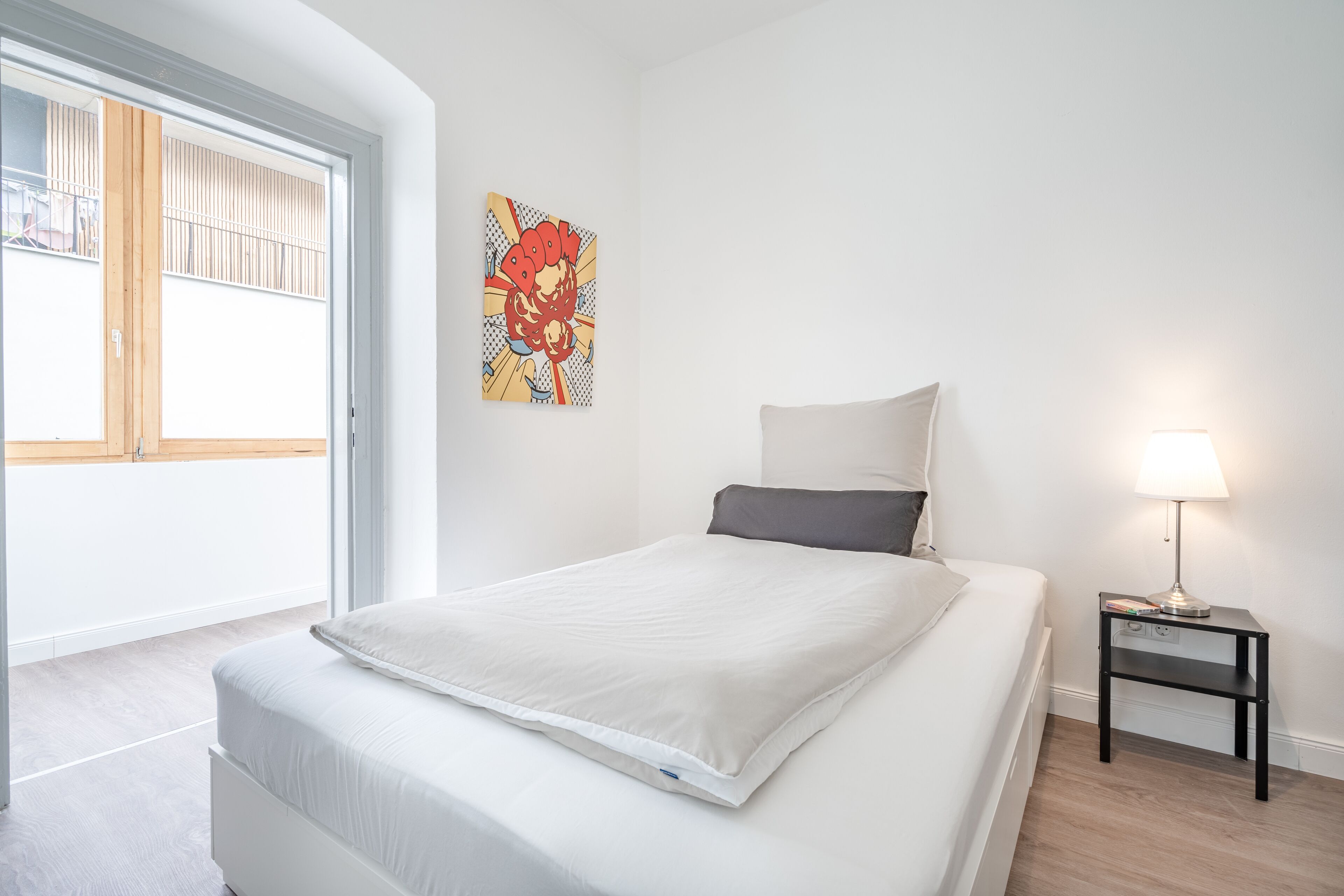A bedroom with a bed, a nightstand, a lamp, and a window with blinds.