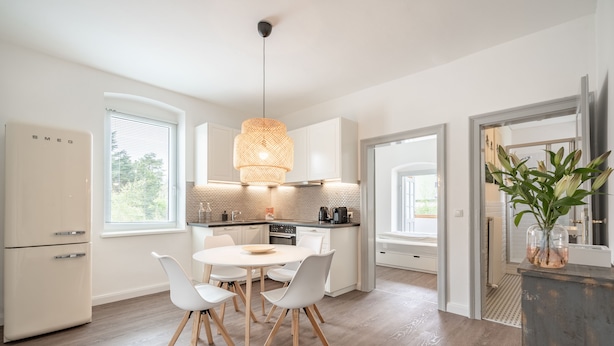 A modern kitchen with white cabinetry, a round dining table with white chairs, and a hanging light fixture.