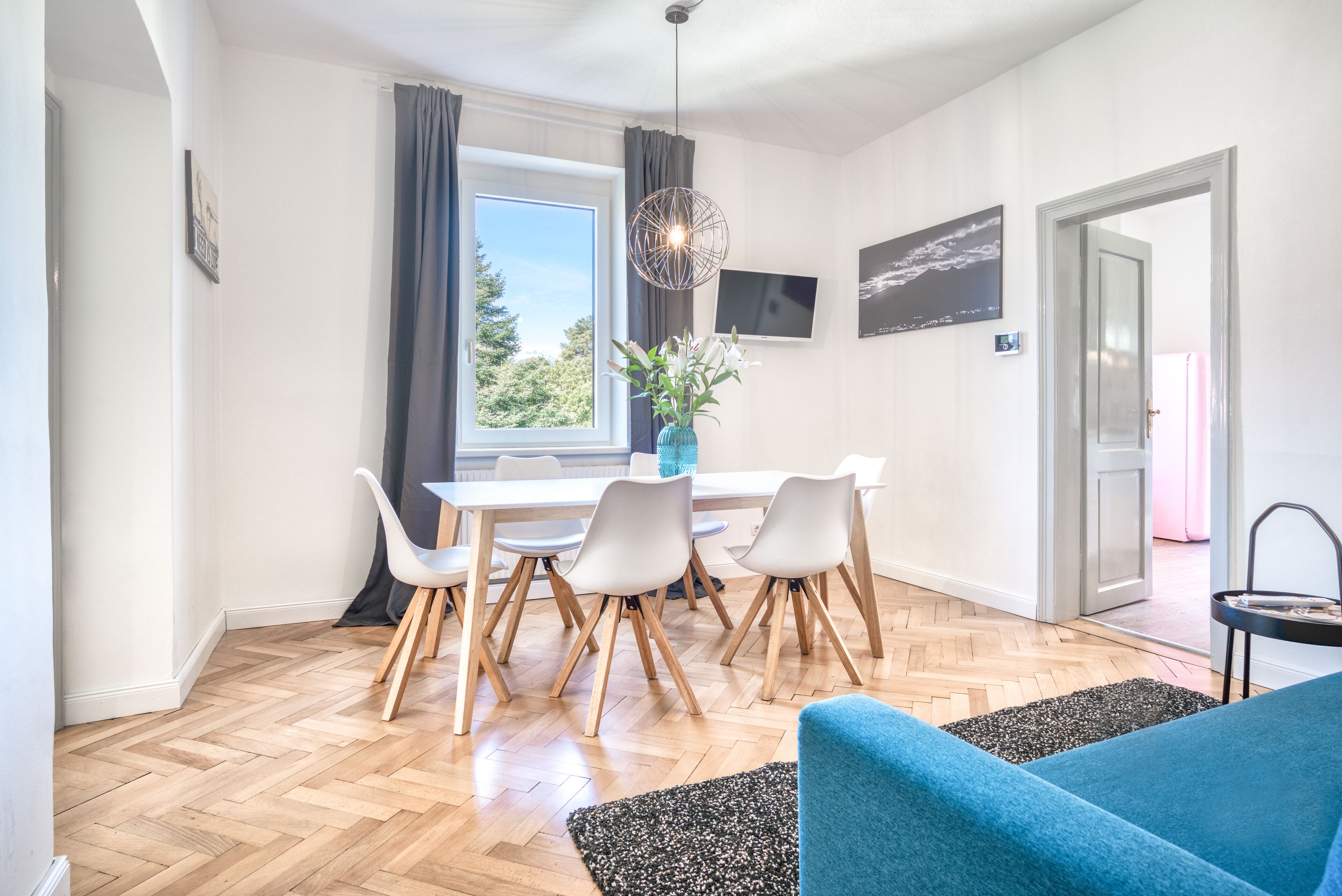 Een moderne eetruimte met een houten visgraatvloer, witte stoelen en een tafel.