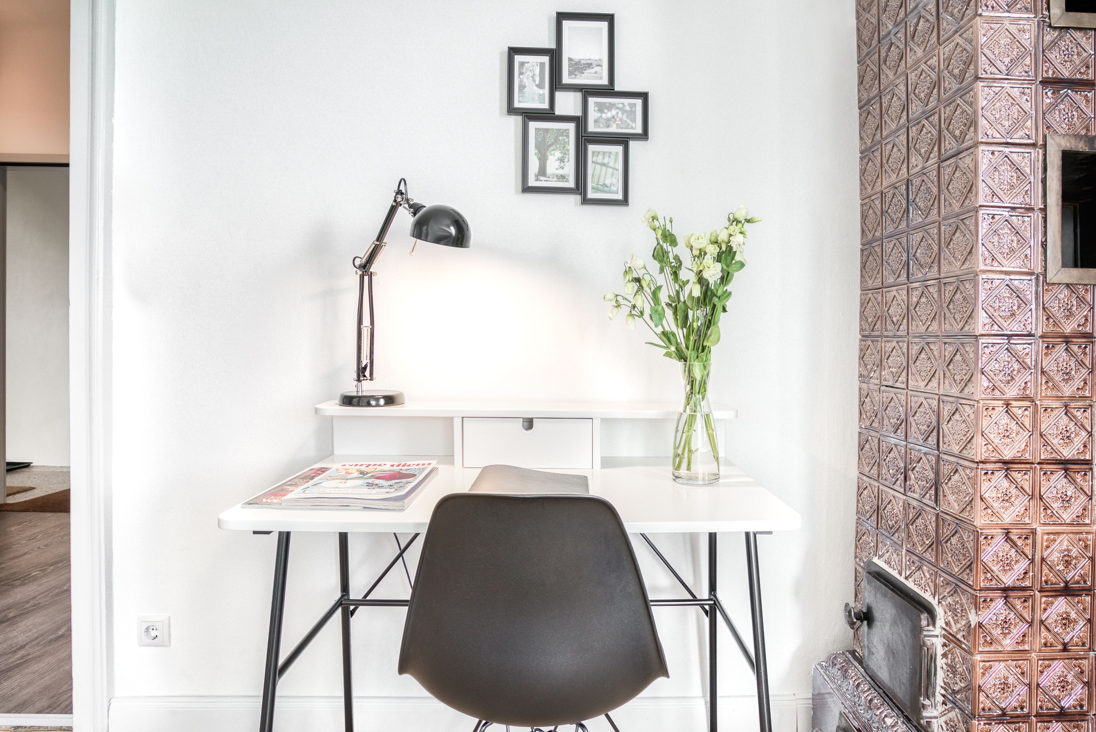 A workspace with a desk, chair, lamp, and framed pictures on the wall.