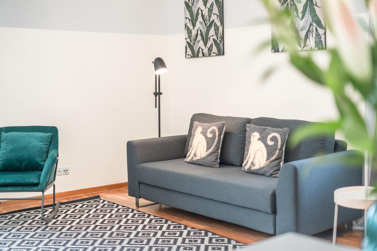 Una sala moderna con un sofá gris, un sillón verde azulado y una alfombra estampada.
