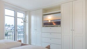 A bedroom with a large bed, a built-in TV, and a view of the sea through a window. - Luxus-hausteil in Beliebter Wohngegend auf ca. 170 m² für bis zu 7 Personen (Wenningstedt-Braderup (Sylt))