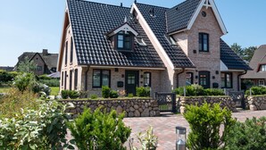 A large brick house with a steeply pitched roof, multiple windows, and a stone wall surrounding the property. - Luxus-hausteil in Beliebter Wohngegend auf ca. 170 m² für bis zu 7 Personen (Wenningstedt-Braderup (Sylt))