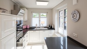 A modern kitchen with white cabinets, a black countertop, and a window with blinds. - Luxus-hausteil in Beliebter Wohngegend auf ca. 170 m² für bis zu 7 Personen (Wenningstedt-Braderup (Sylt))
