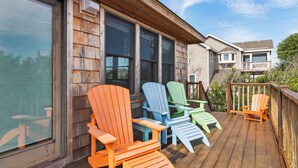 Een houten terras met kleurrijke Adirondack-stoelen en een houten leuning.