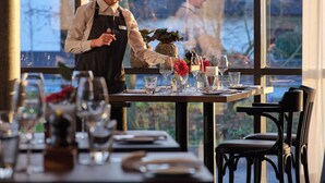 A restaurant with a large window, a table set with wine glasses, plates, and cutlery, and a person standing by the window.