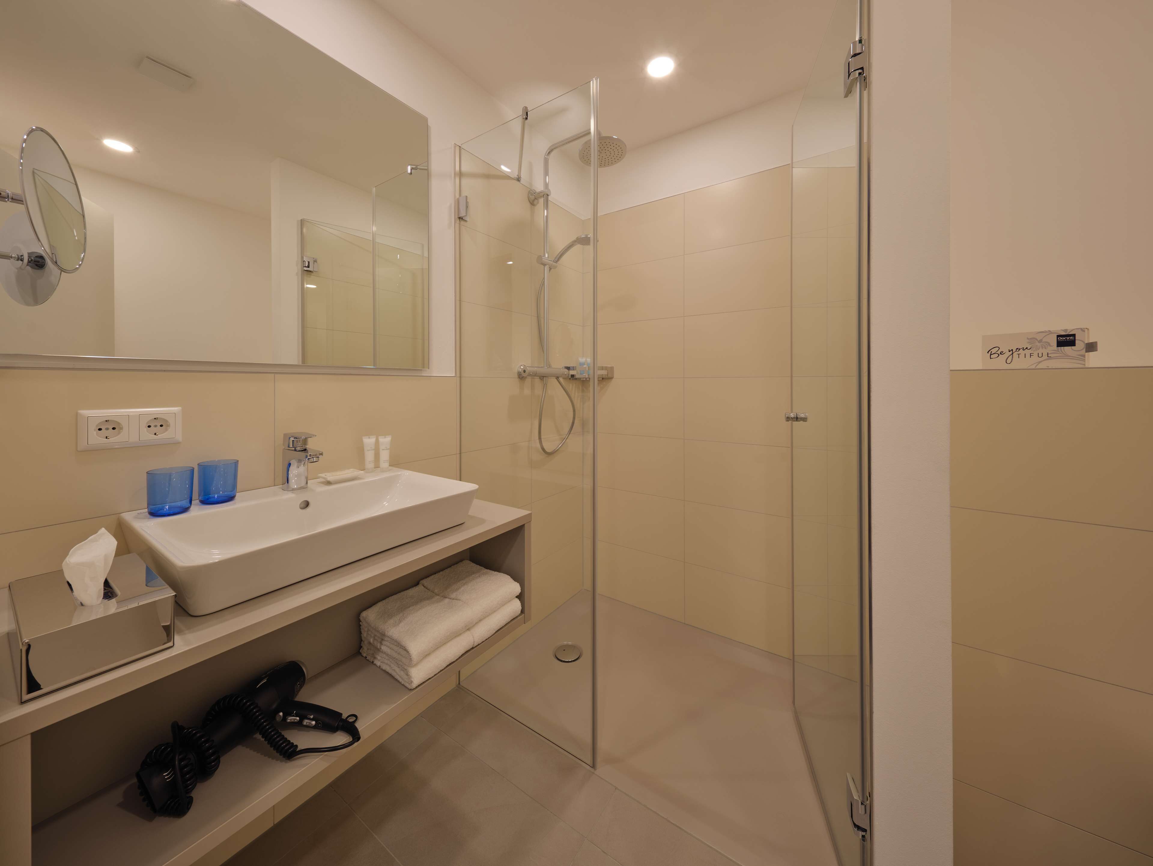 A modern bathroom with a glass-enclosed shower, a white sink, and a mirror.