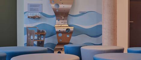 Un área de descanso moderna con asientos azules y blancos, una escultura de pared única y una lámpara colgante.