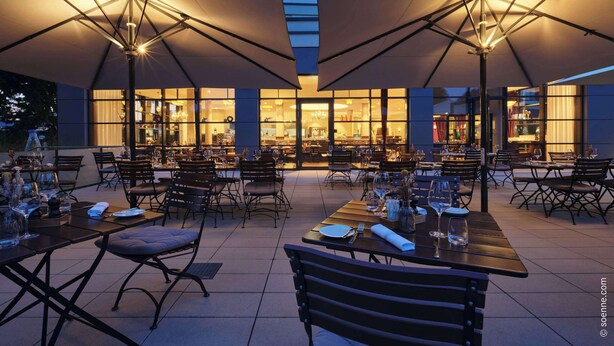 An outdoor dining area with tables and chairs, large umbrellas, and a building with large windows in the background.