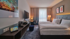 A hotel room with a large bed, a desk with a computer, a TV, and a painting of a Ferris wheel.