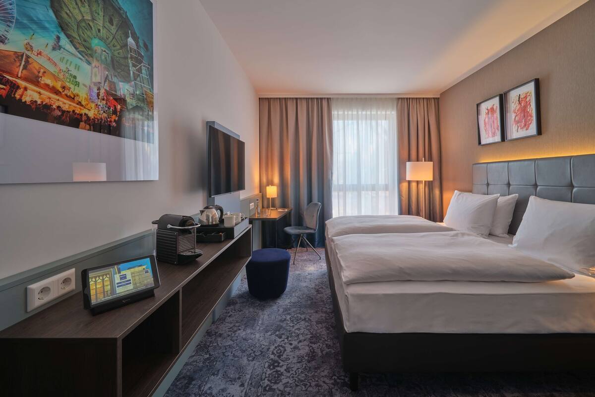 A hotel room with a large bed, a desk with a computer, a TV, and a painting of a Ferris wheel.