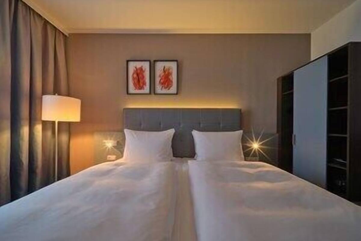 A hotel room with a double bed, a nightstand with a lamp, a wardrobe, and two framed pictures on the wall.