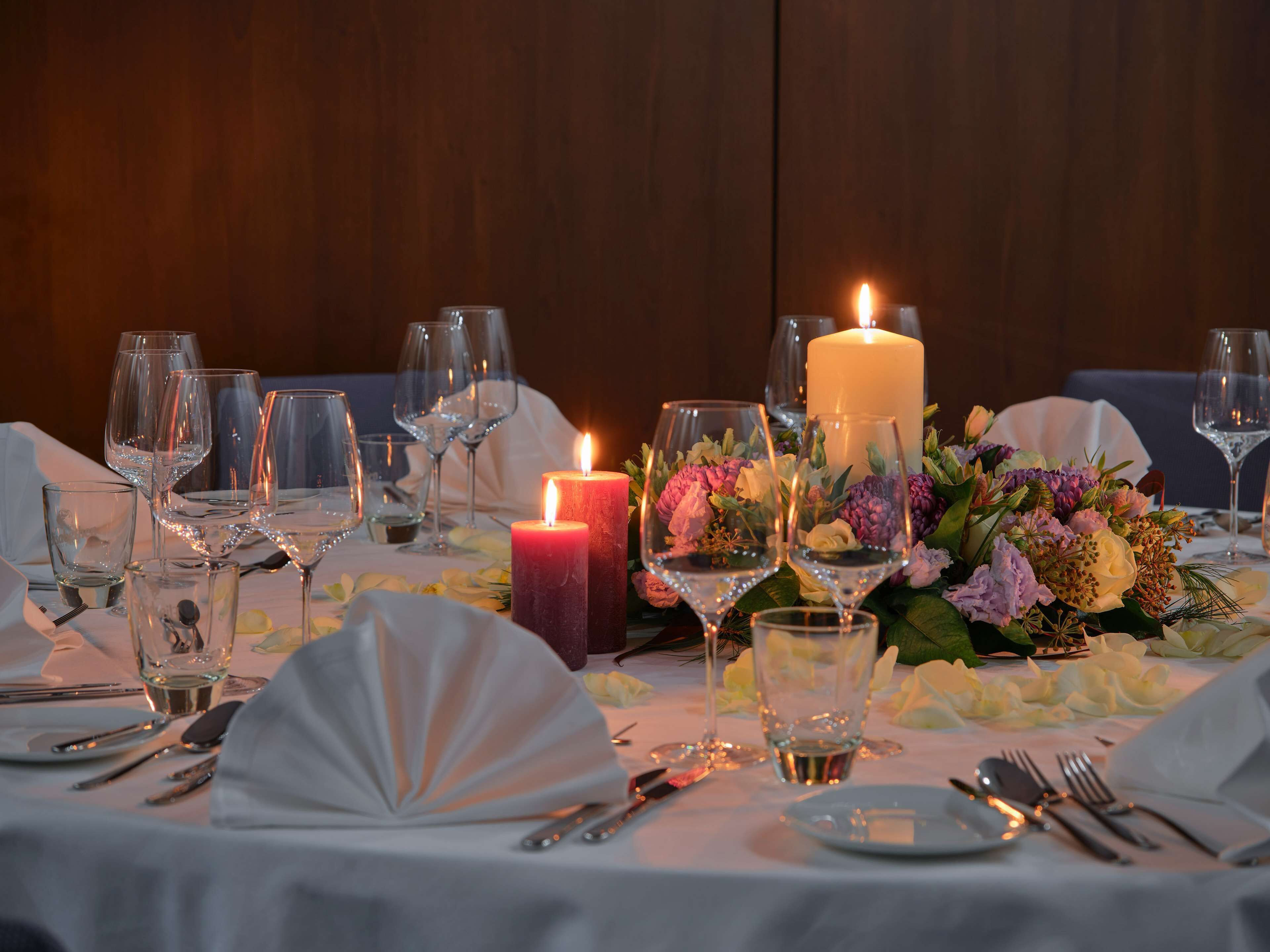 A table set for a formal dinner with wine glasses, plates, cutlery, a candle, and a floral centerpiece.